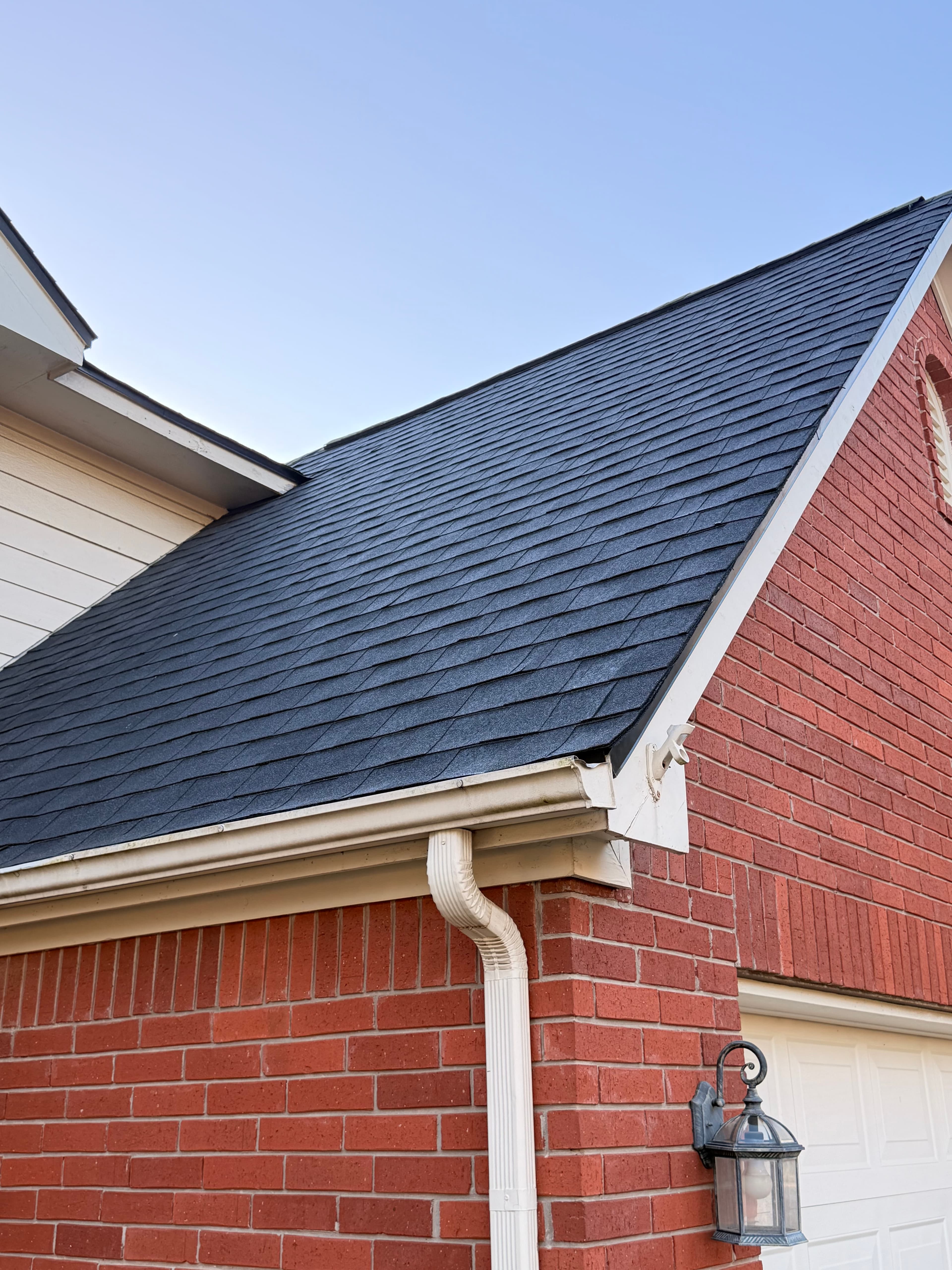 Upward view of a red brick house with dark shingles, white gutters, and a lantern.