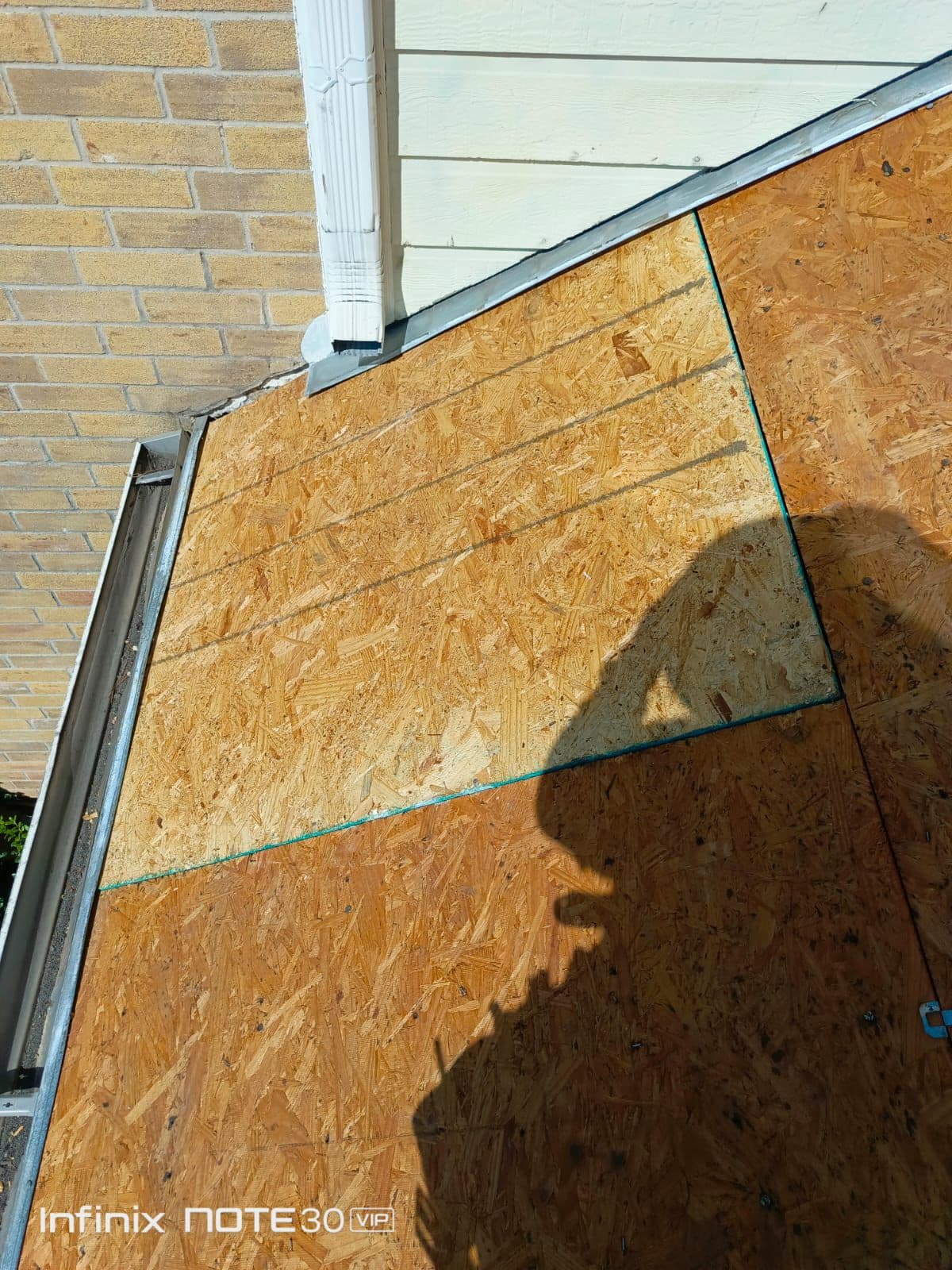 Sloped roof covered in OSB sheathing next to a brick wall and white siding.